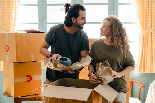 Free Multiethnic couple packing ceramic belongings in parchment before relocation Stock Photo