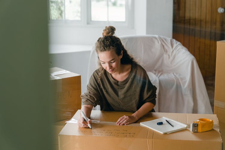 Woman Signing Box With Marker While Sitting In Living Room