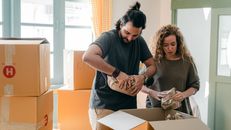 Diverse couple packing belongings in parchment near different boxes indoors