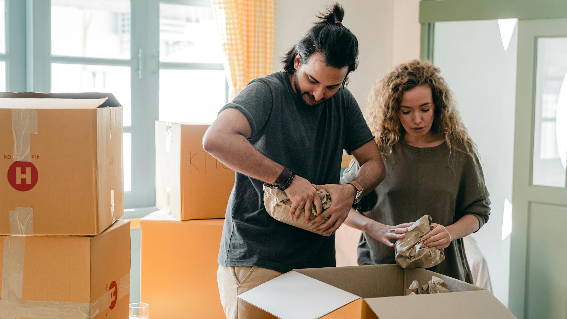 Diverse couple packing belongings in parchment near different boxes indoors