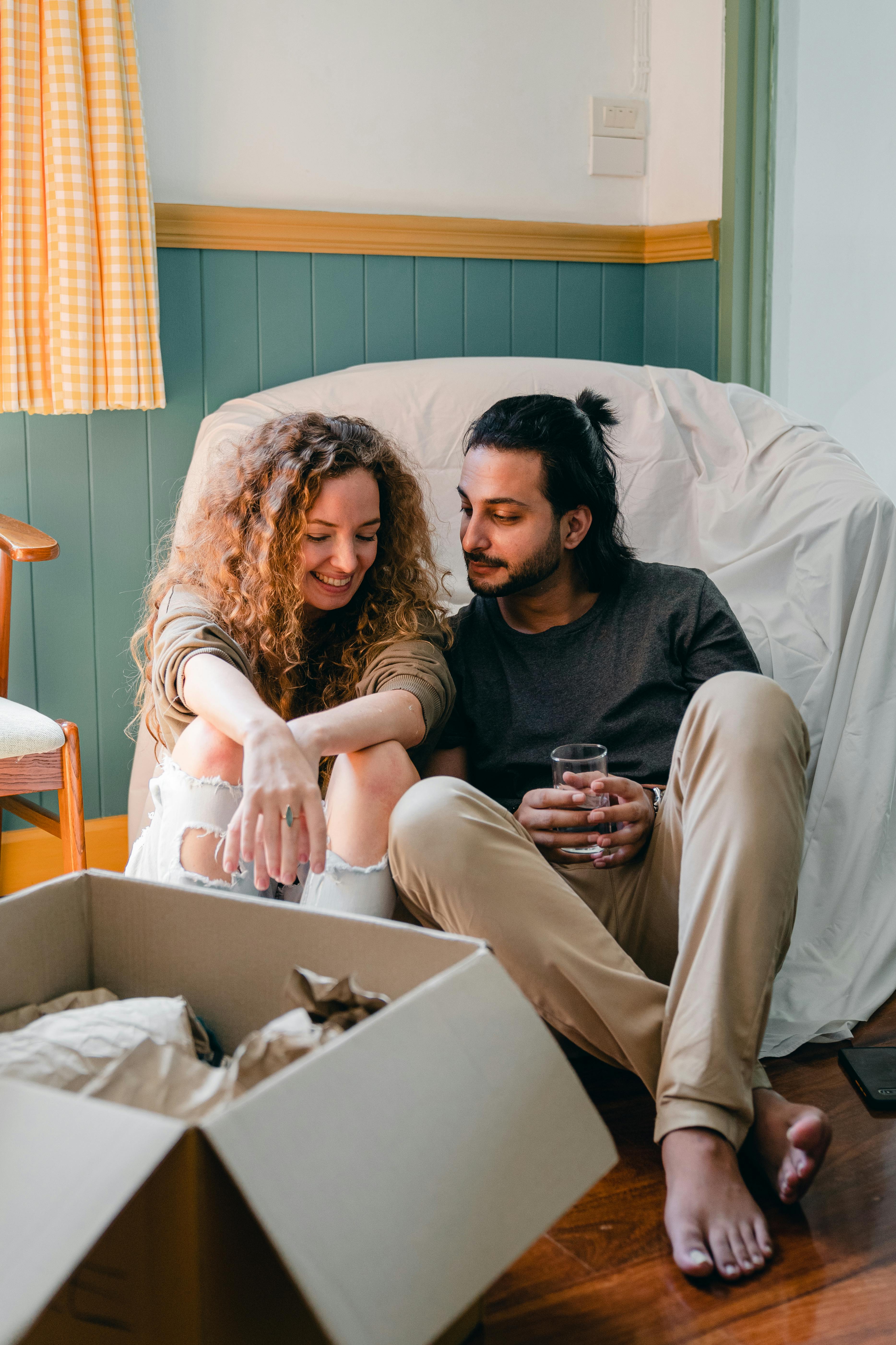 Positive multiethnic couple chatting while sitting in room and packing · Free Stock Photo