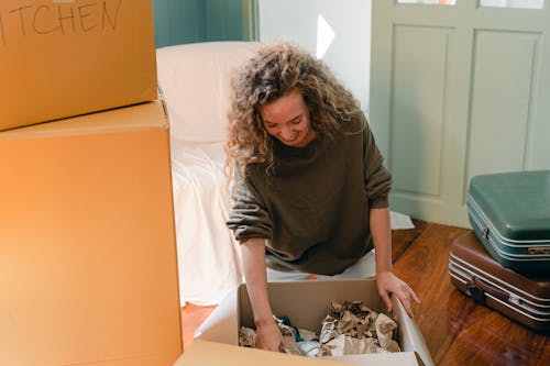 Happy woman unpacking carton box in living room