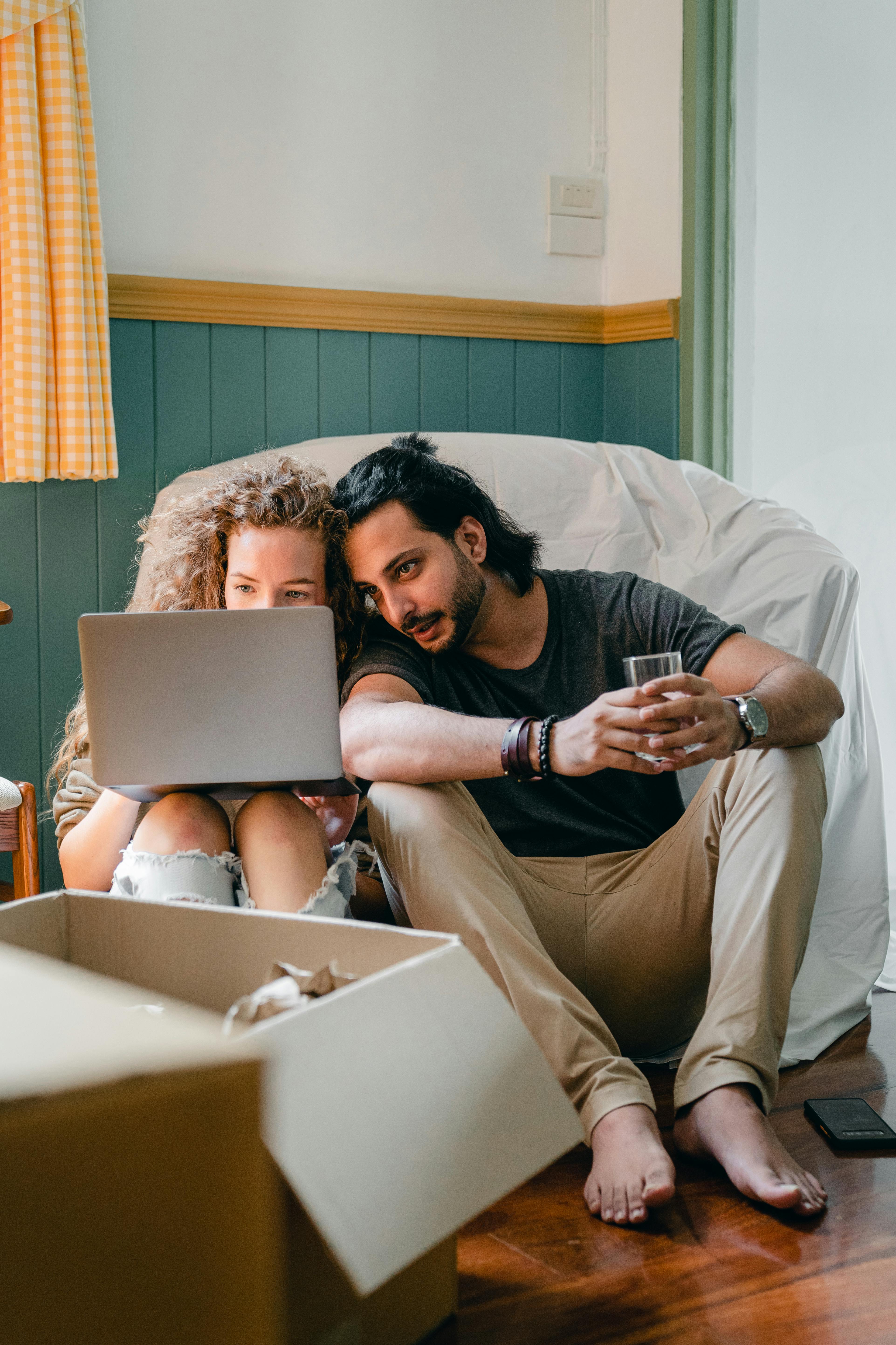 positive couple using laptop near carton boxes