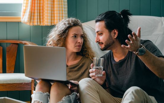 Pensive couple with laptop sitting on floor