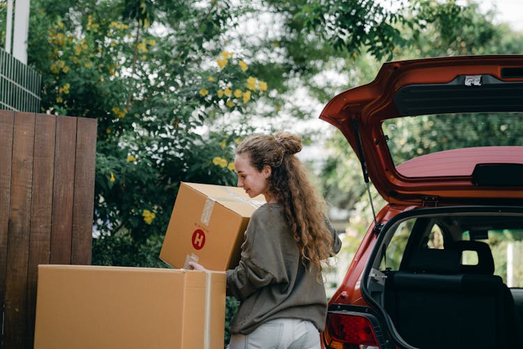 Young Woman Carrying Box To New Home While Unpacking Car