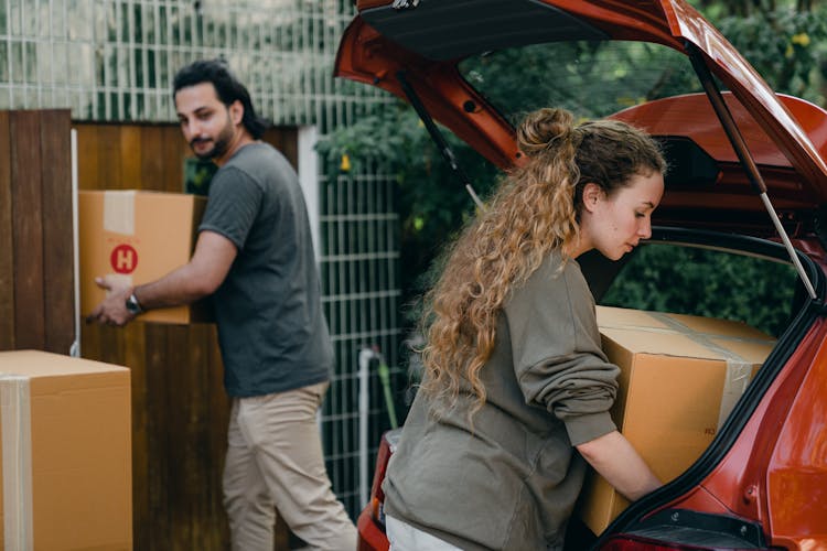 Young Couple Unpacking Car In Yard Of New House