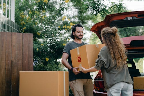 Free Boyfriend and girlfriend in casual wear helping each other with unpacking car while moving in together on sunny summer day Stock Photo