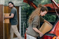 Multiethnic young couple in casual wear taking carton boxes out of automobile trunk near newly bought house on summer day