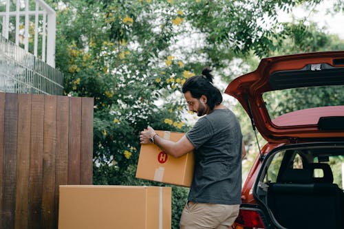 Free Young male taking boxes out of luggage boot of car Stock Photo