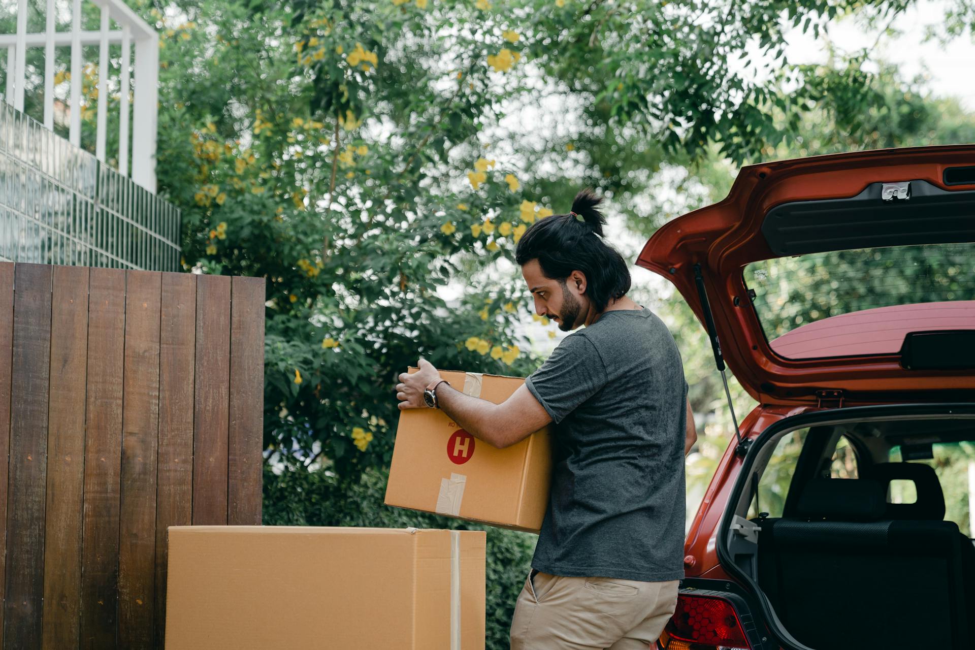 Young male taking boxes out of luggage boot of car