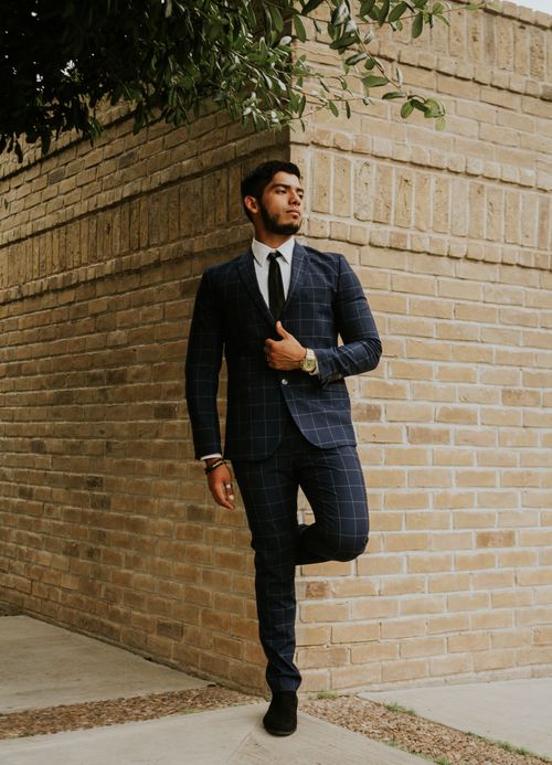 Free Full body of contemplative ethnic male in stylish outfit leaning with leg on old shabby brick wall under tree on city street and looking away Stock Photo