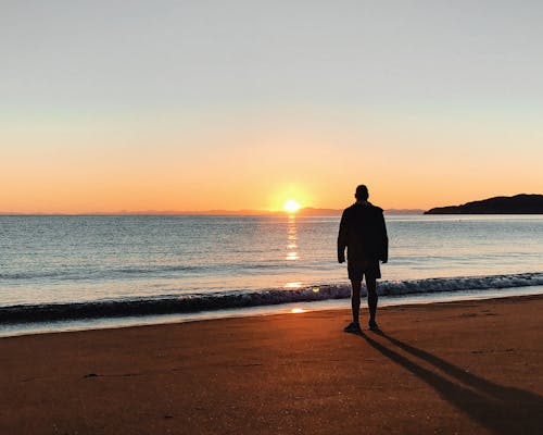 Silhouette of Man Standing on Beach during Sunrise