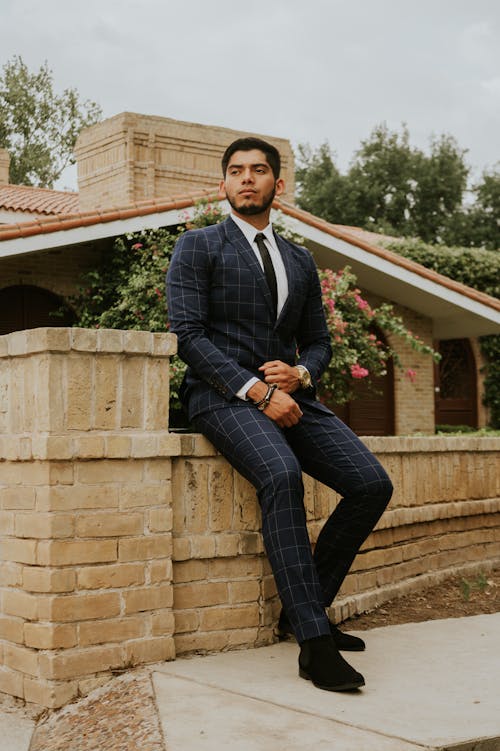 Handsome ethnic man in formal suit sitting on brick fence