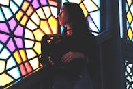 一位女子站在彩色玻璃窗旁，散发着沉思而优雅的气质