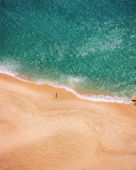 A tranquil aerial view of Nazaré Beach, Portugal, featuring a lone walker on the sandy shore.