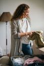 Cheerful young female packing suitcase in bedroom while moving house