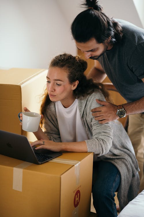 Young couple using laptop in room full of packed boxes