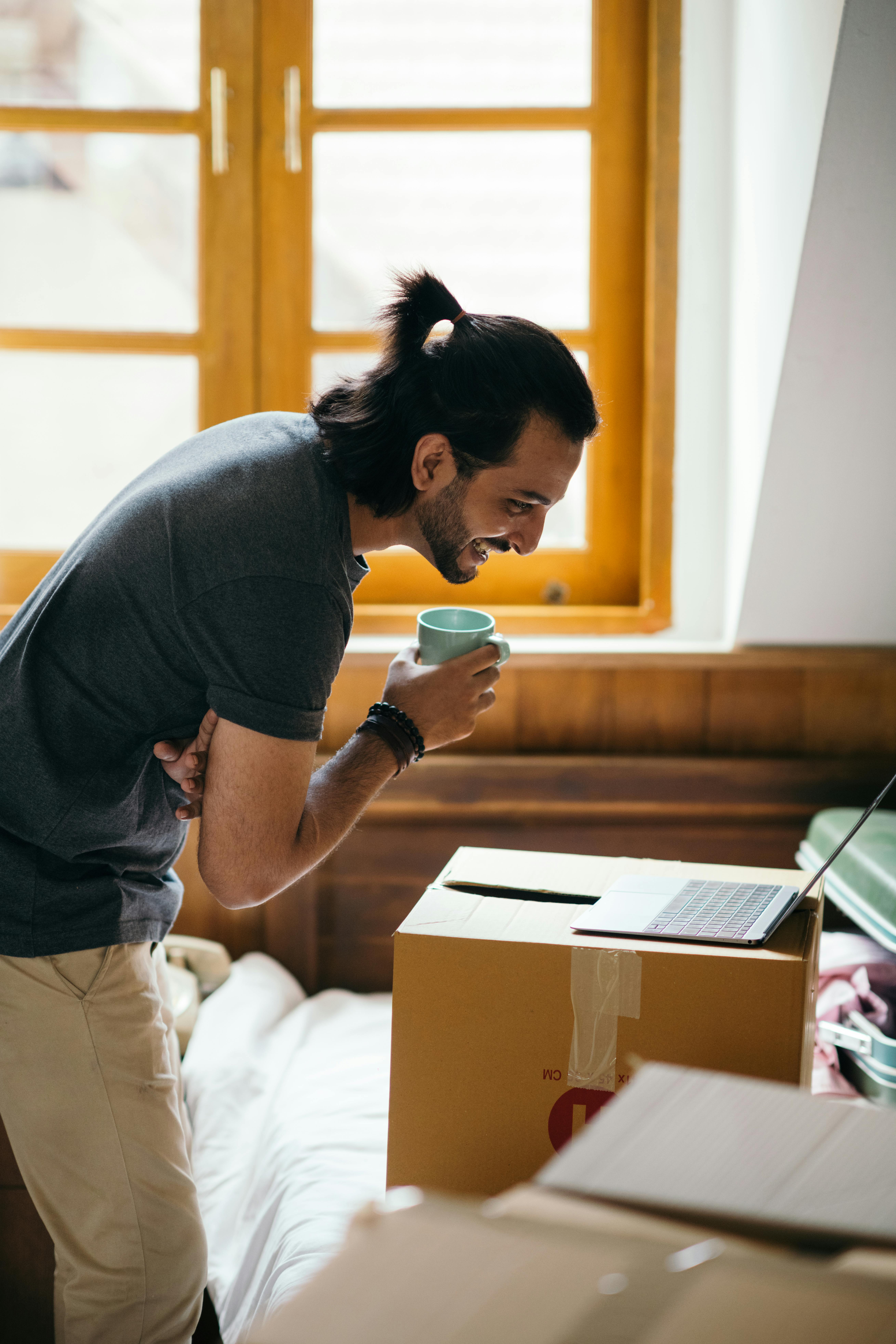 cheerful man with coffee using laptop in new house