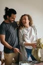 Young multiracial man and woman laughing happily at contents of travel suitcase in bedroom while packing clothes for journey