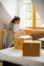 Serious female with curly hair carefully packing stuff in boxes preparing for moving out light apartment