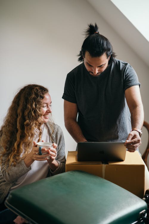 Cheerful couple using laptop while packaging stuff