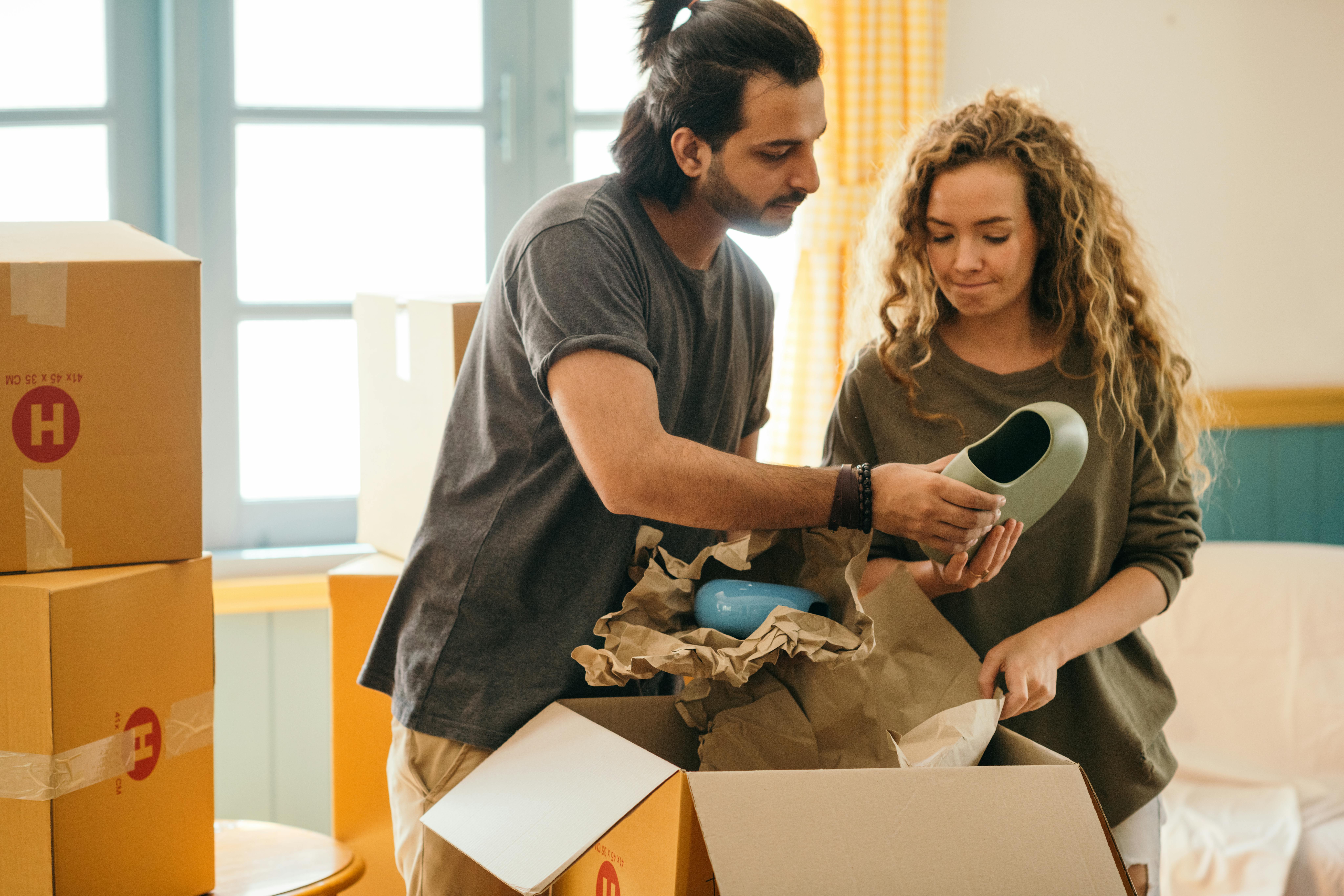 pensive multiracial couple unpacking vase after renting new apartment