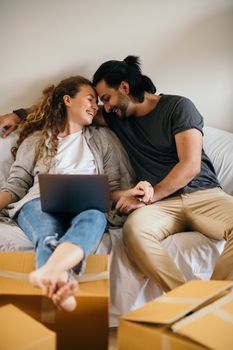 笑着的夫妇在新家的搬家箱旁，拿着笔记本电脑放松身心，一起迎接新的开始
