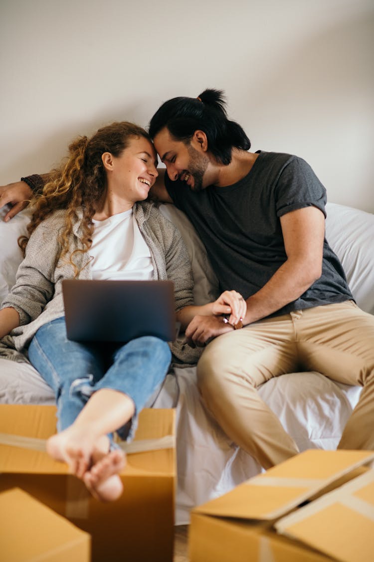 Smiling Couple Resting On Sofa With Laptop After Unpacking Boxes