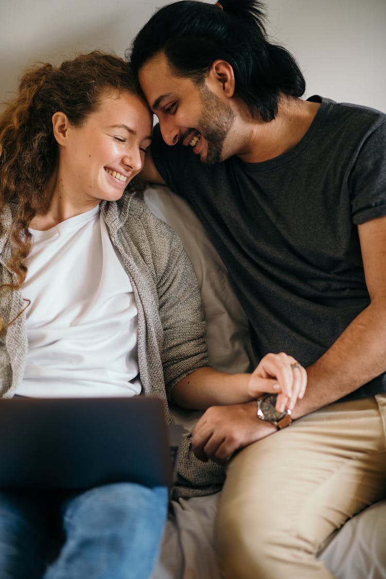 Happy Multiethnic Couple Using Laptop While Sitting On Sofa