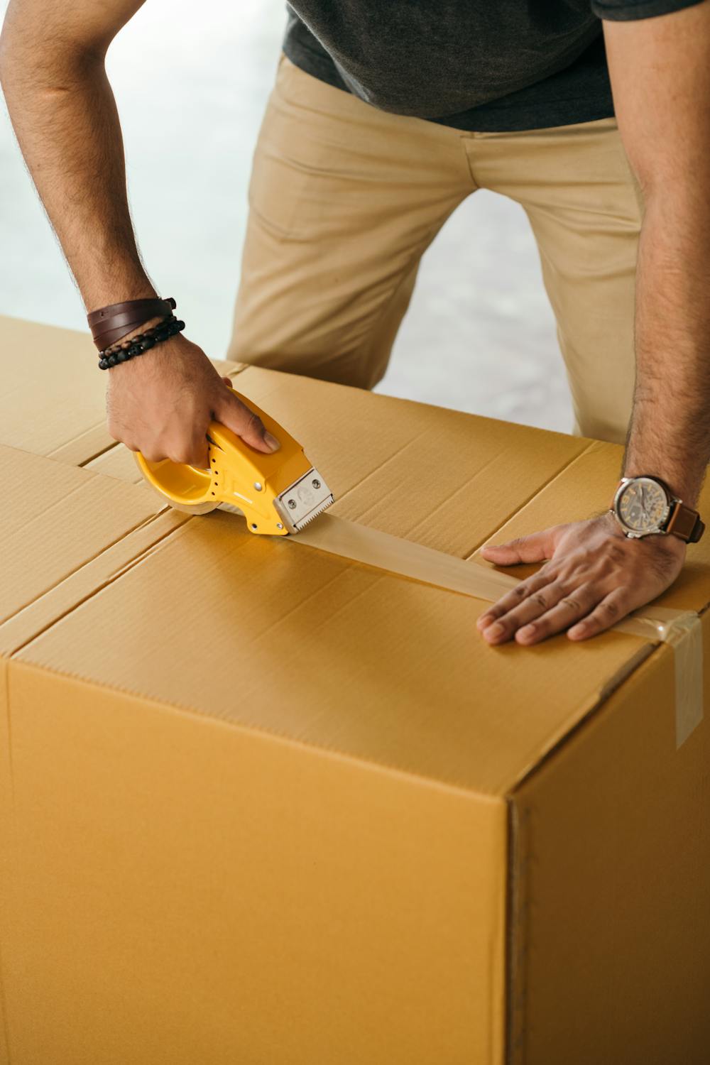 Man from a packing and moving company sealing a box with Scotch tape