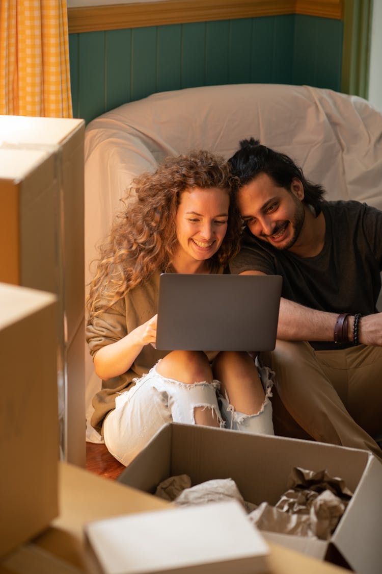 Happy Diverse Couple Using Laptop While Relocating Into New Apartment