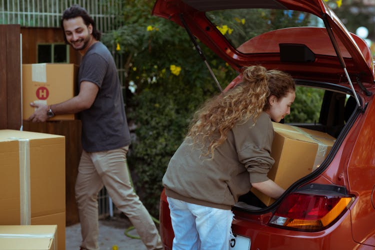 Diverse Couple Taking Carton Boxes Out Of Red Car While Relocating In New House