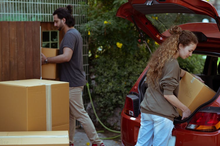 Diverse Couple Getting Carton Boxes Out Of Car While Relocating In Suburb Or Countryside