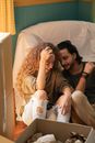 Happy couple sitting on floor and talking among boxes and covered armchair