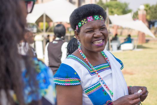 Smiling woman wearing traditional South African clothing enjoying an outdoor event.
