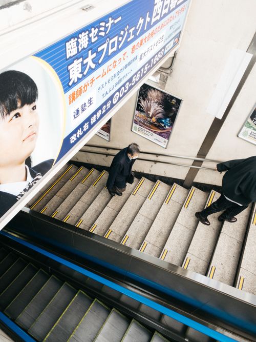 Free From above of contemporary style moving staircase near unrecognizable crop man and woman climbing up stairs under bright signboard with hieroglyphs and photo in building Stock Photo