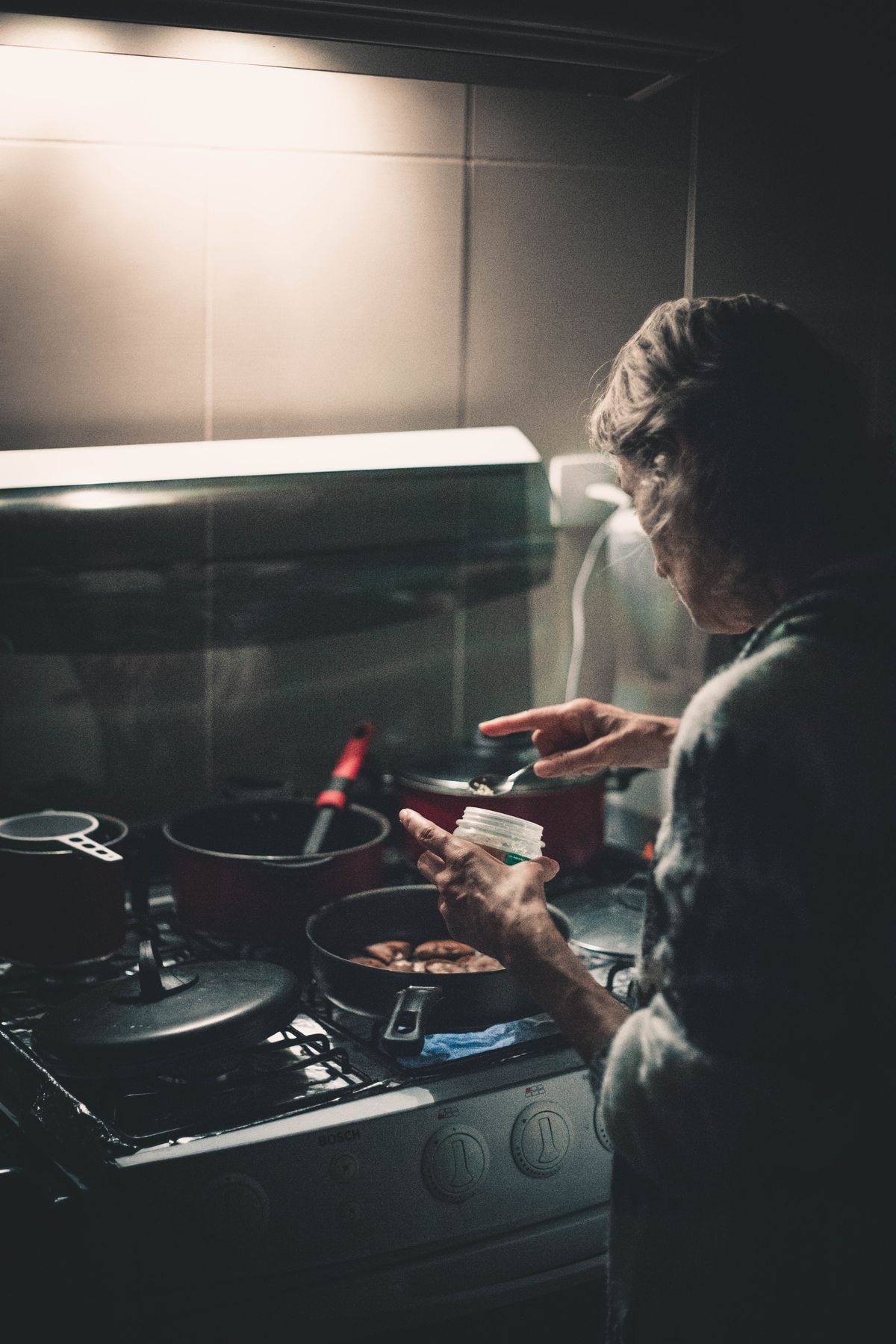 A person cooking dinner in a home kitchen, captured from behind. Illustrative editorial photograph.