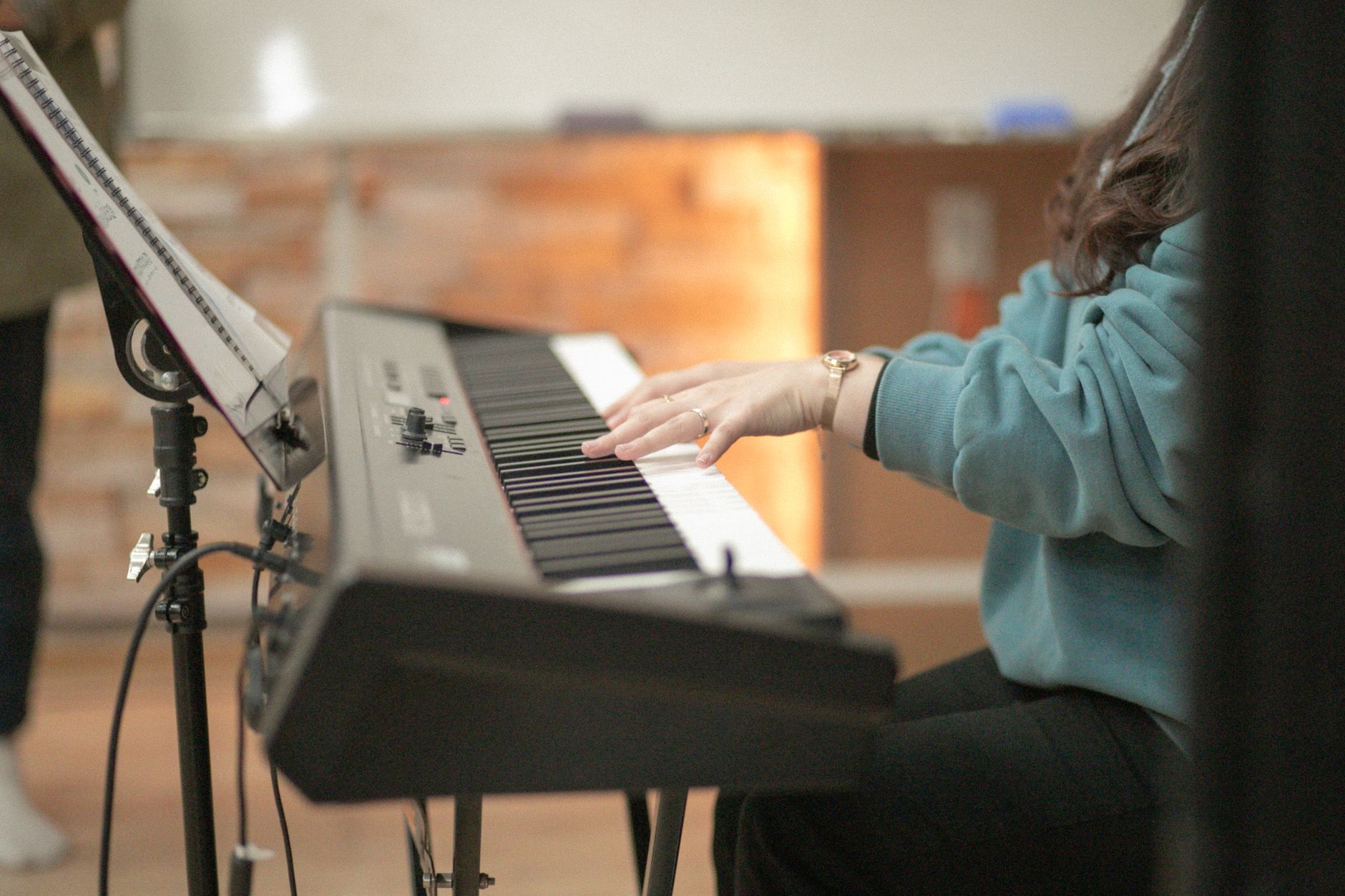 A person in a blue jacket plays an electronic keyboard indoors, creating a cozy musical vibe.