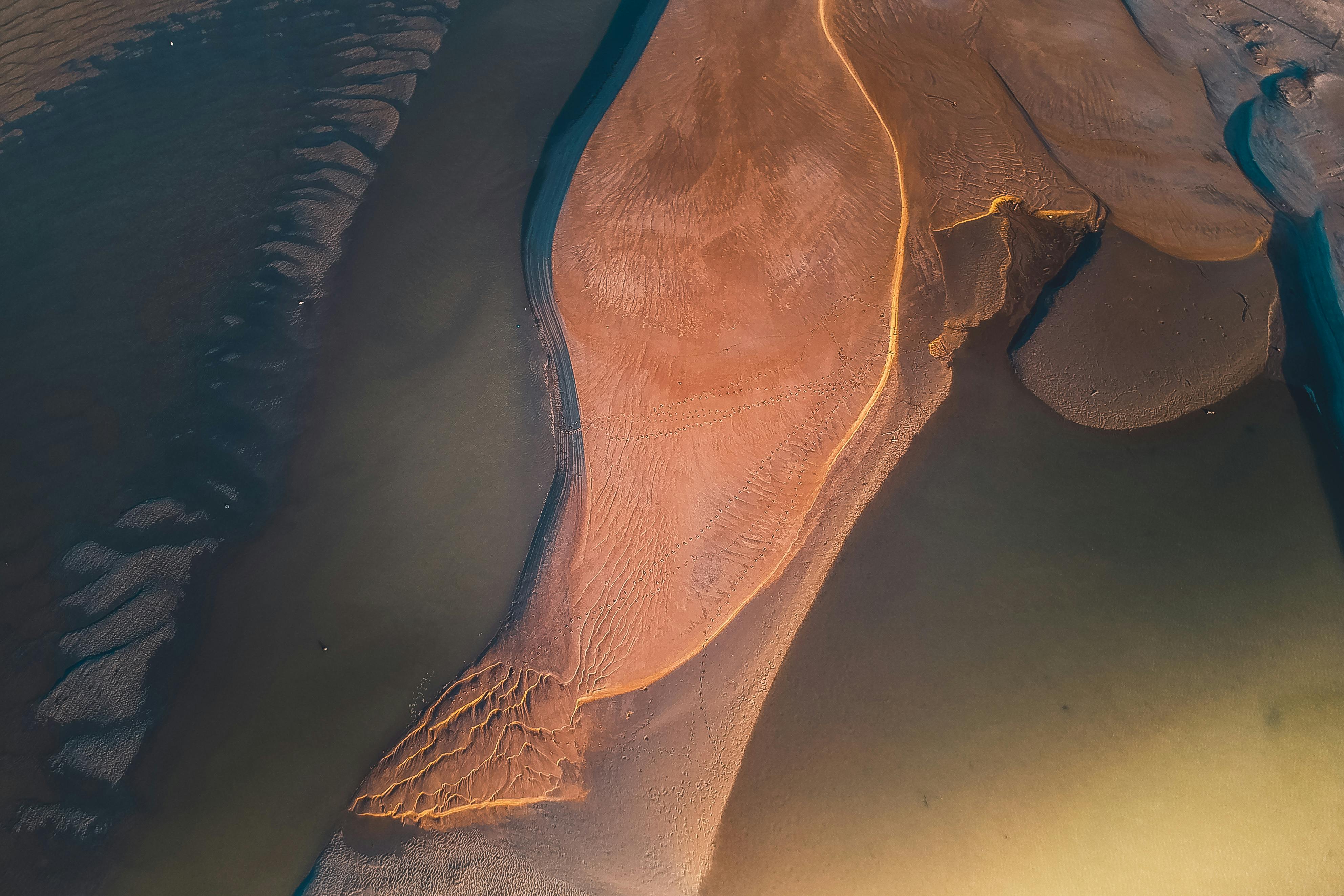 Drone view of sandy rough peninsula washed with water in sunny day