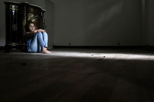 Free A woman sits alone in a dark room, highlighting solitude and introspection. Stock Photo