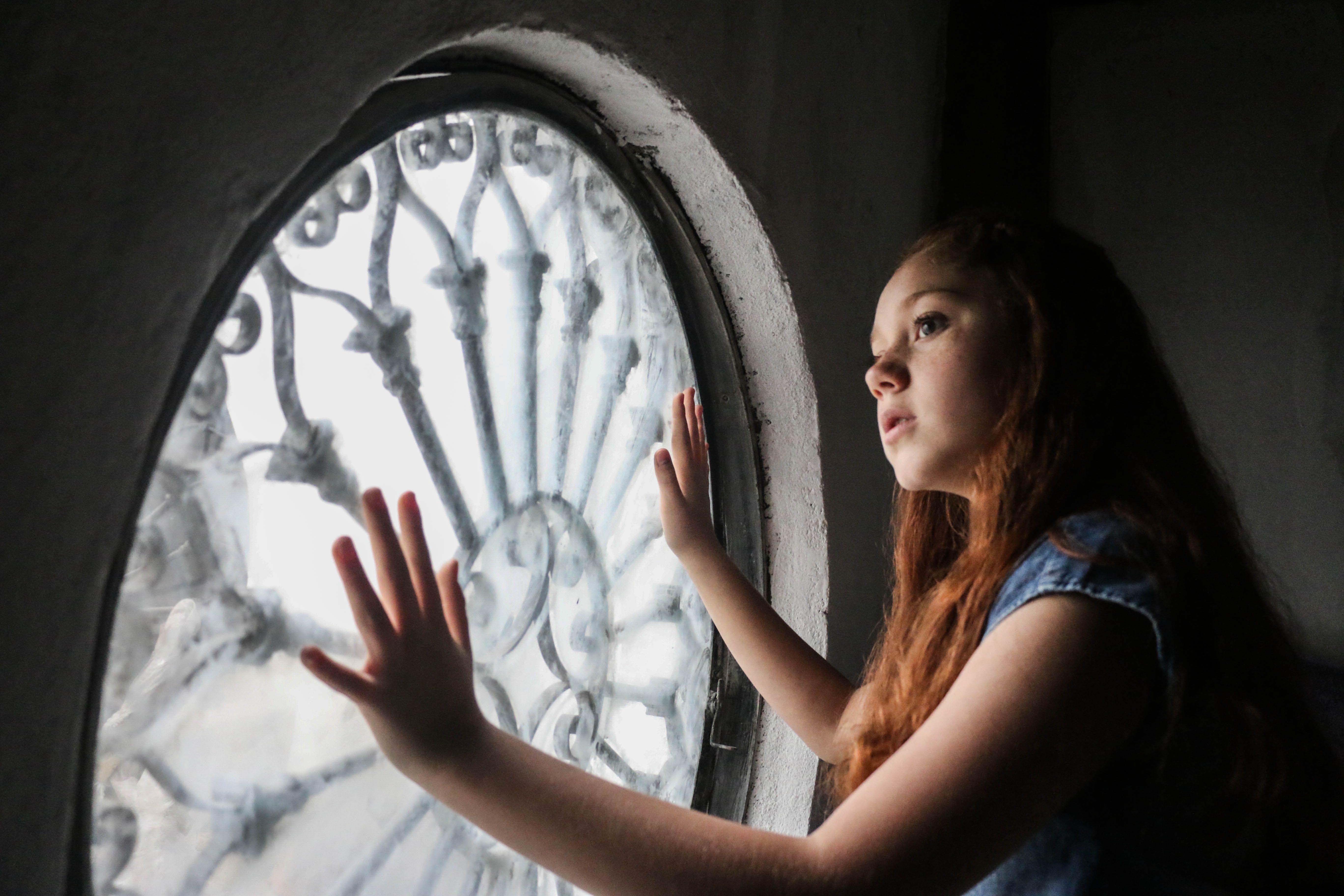 Young woman gazing out of an ornate circular window, lost in thought.