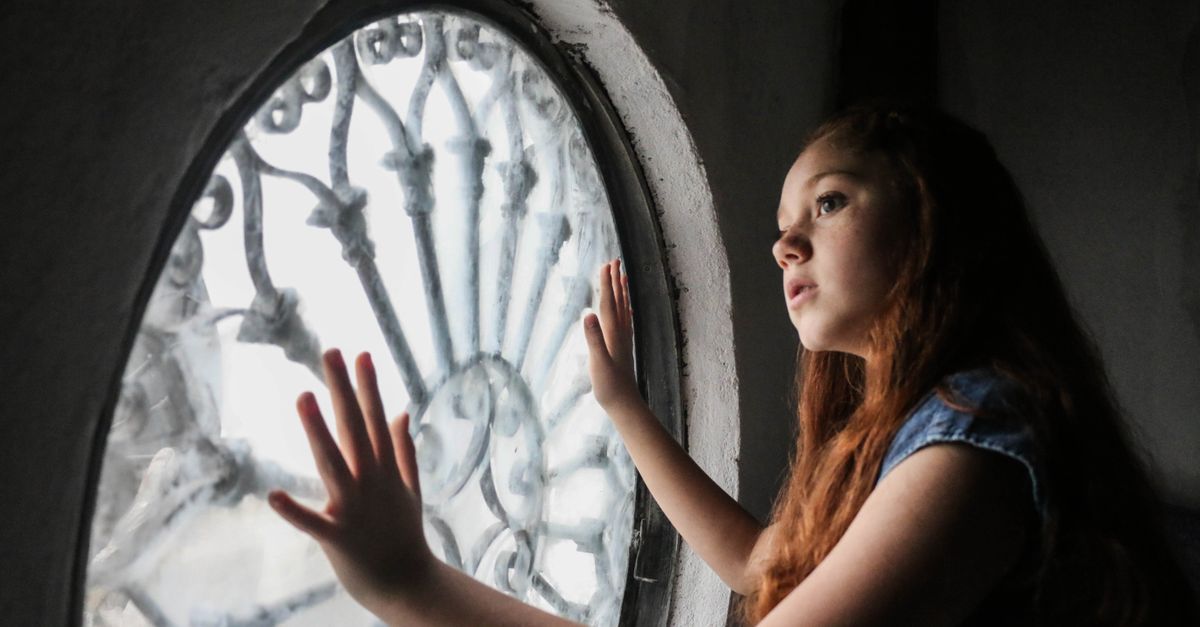 Young woman gazing out of an ornate circular window, lost in thought.