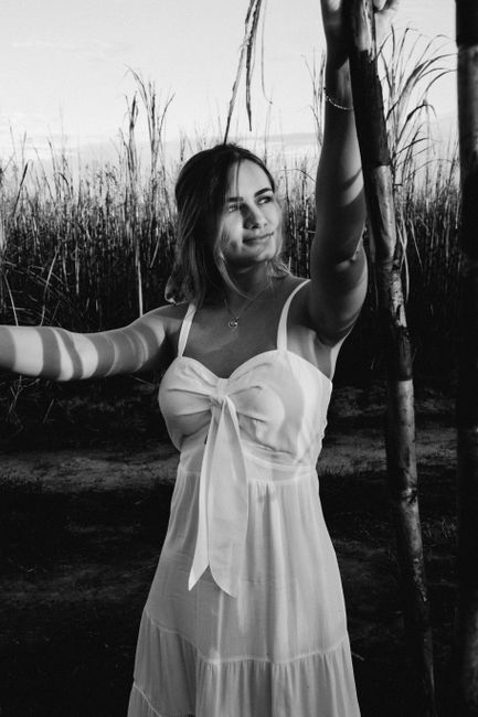 Black and white of content female in white sundress standing in grass in sunny day and looking away pensively