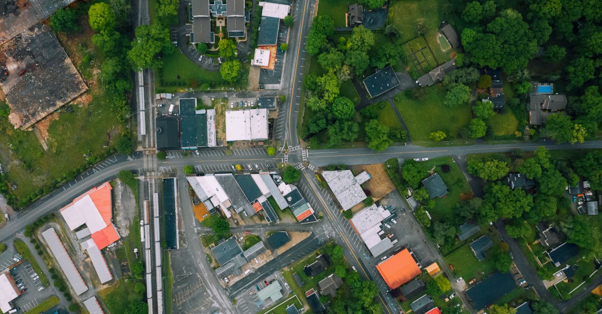 Drone view outpost town district with contemporary cottages and large industrial buildings surrounded with lush tree on summer day