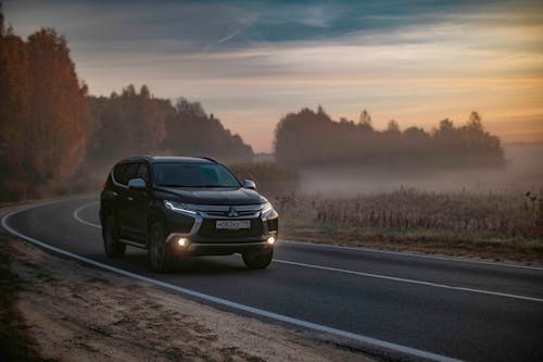 Contemporary black offroader car driving along asphalt road in peaceful foggy countryside area in dusk