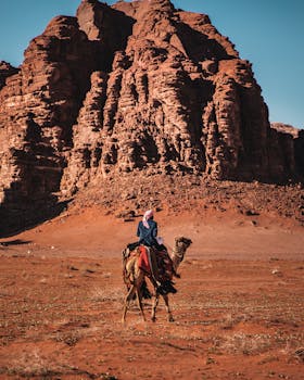 在约旦瓦迪穆萨风景优美的沙漠中，一名男子骑着骆驼，展示了引人注目的岩石结构