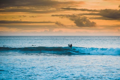 Silhouette of unrecognizable surfer riding surfboard on waving sea surface during picturesque sunset in tropical resort