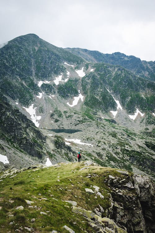 Person Standing on Cliff Across the Mountains