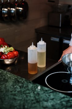 A professional kitchen setup featuring cooking oils and fresh vegetables on a countertop.