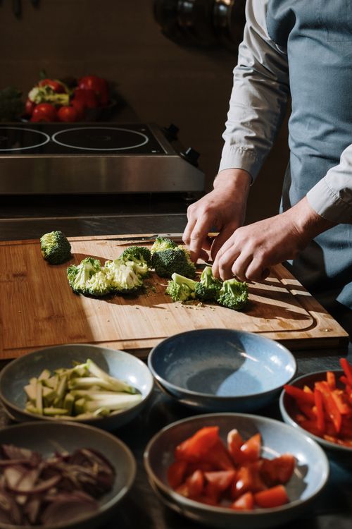 Free Chef chopping broccoli on wooden board with fresh ingredients in bowls for a healthy meal. Stock Photo